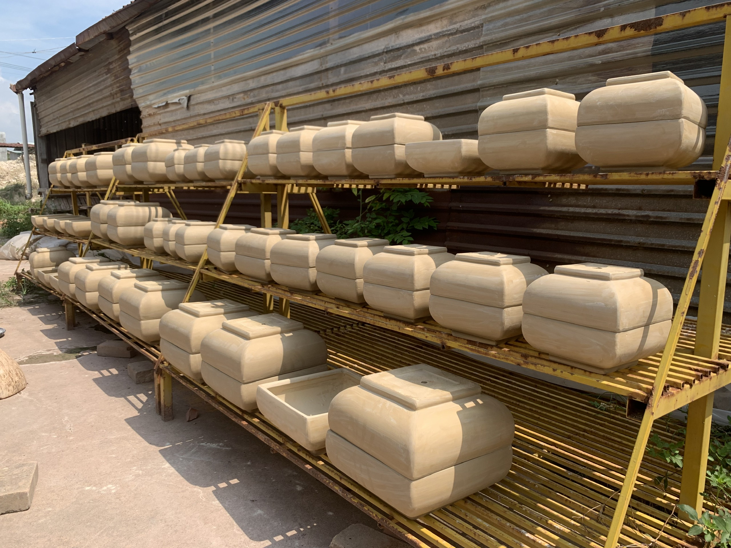 Rows of unfired clay vessels drying on racks